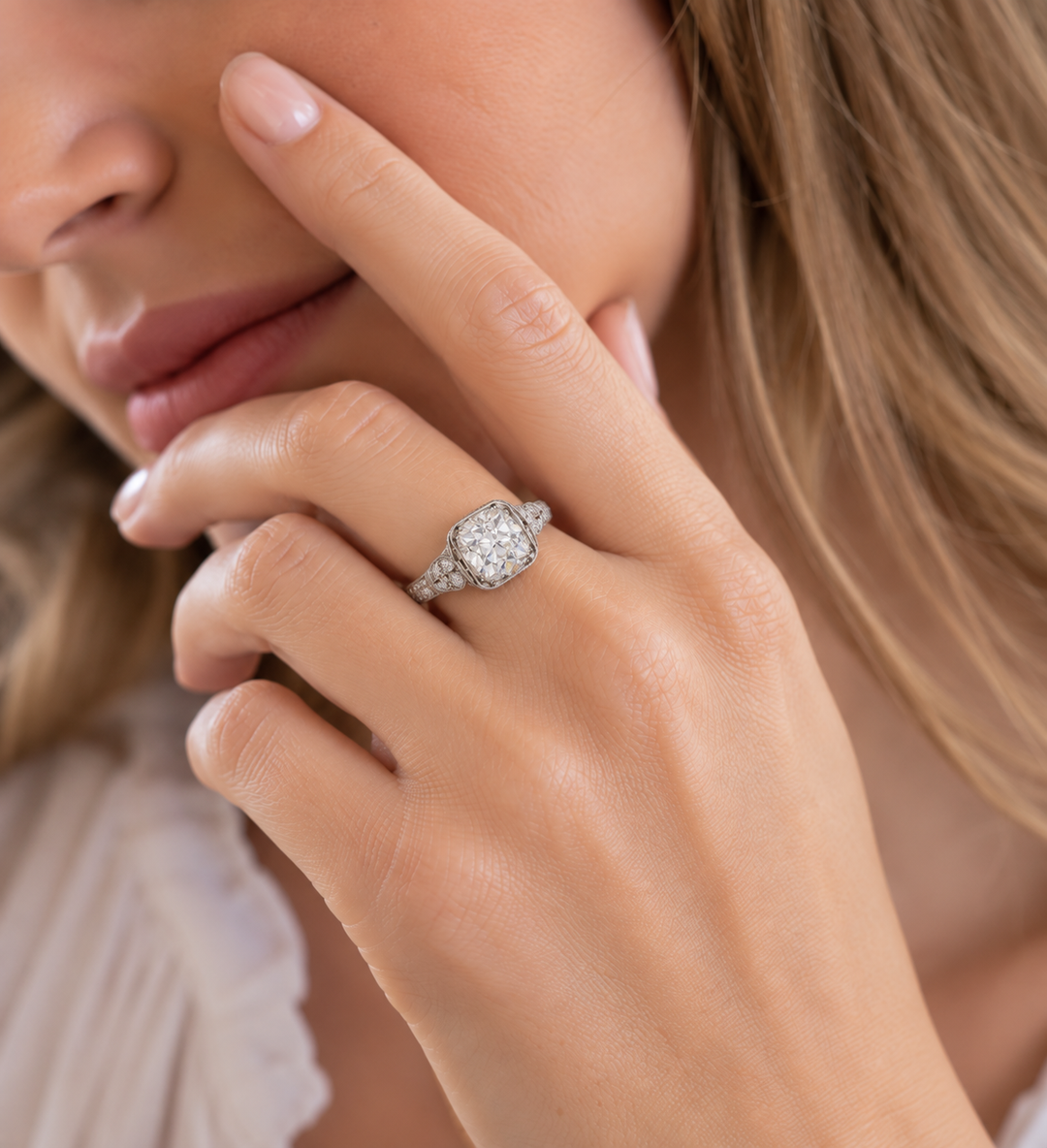 Woman wearing a vintage-style diamond engagement ring with a cushion-cut center stone and detailed platinum setting.