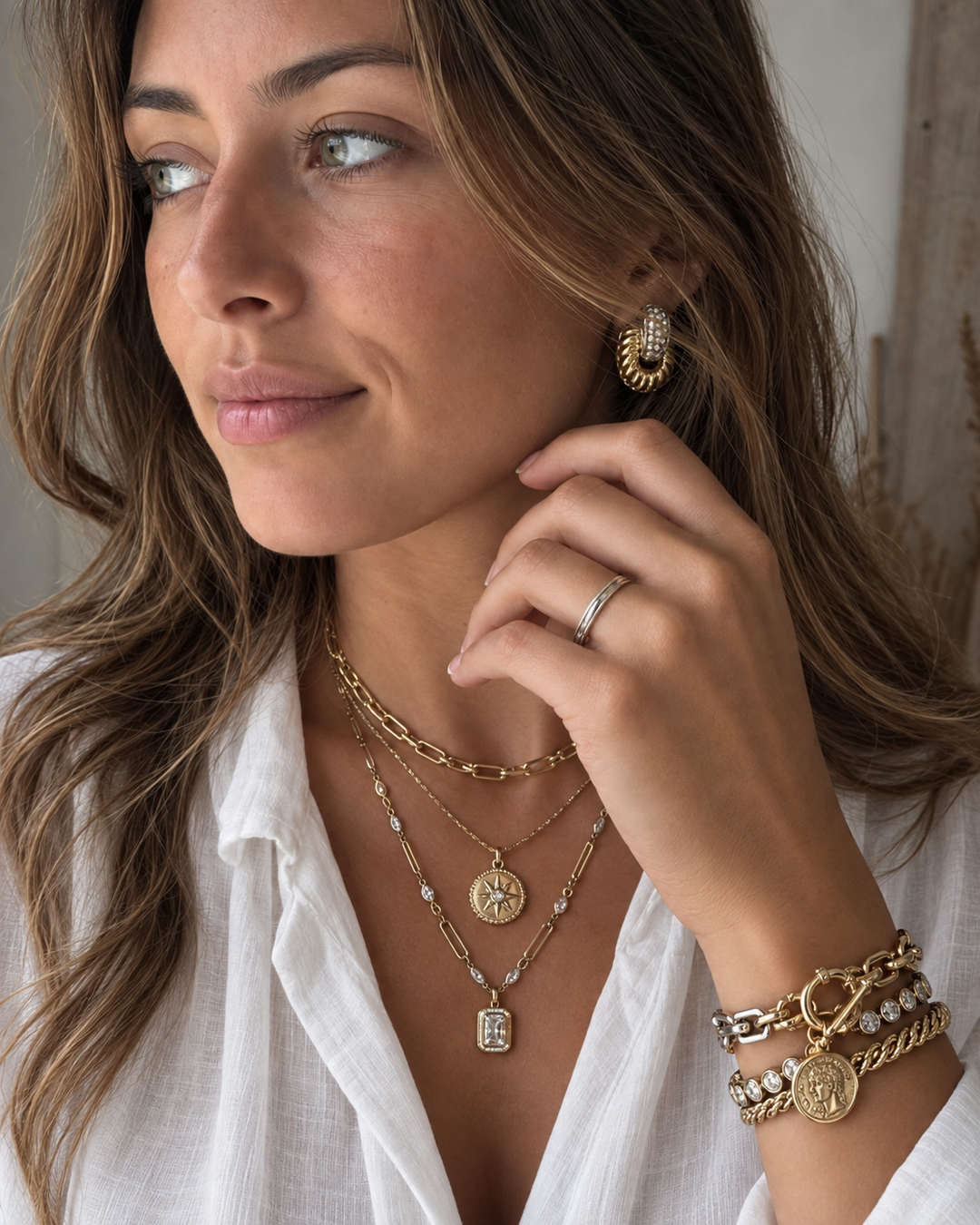 Woman wearing layered gold and diamond necklaces with statement earrings and stacked gold bracelets.